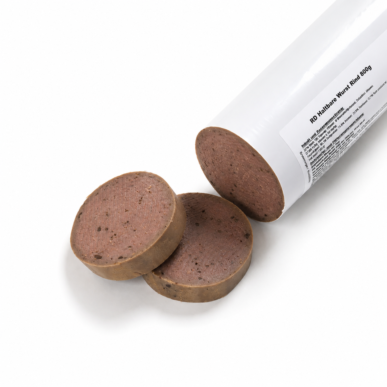 Eine angeschnittene haltbare Rinderwurst für Hunde (800 g) in einer weißen Wursthülle liegt auf einem weißen Hintergrund. Vor der Wurst befinden sich zwei dicke Scheiben, die die feine, schnittfeste Konsistenz der Trainingswurst zeigen. Ein weicher, natürlicher Schatten sorgt für eine realistische Produktdarstellung.