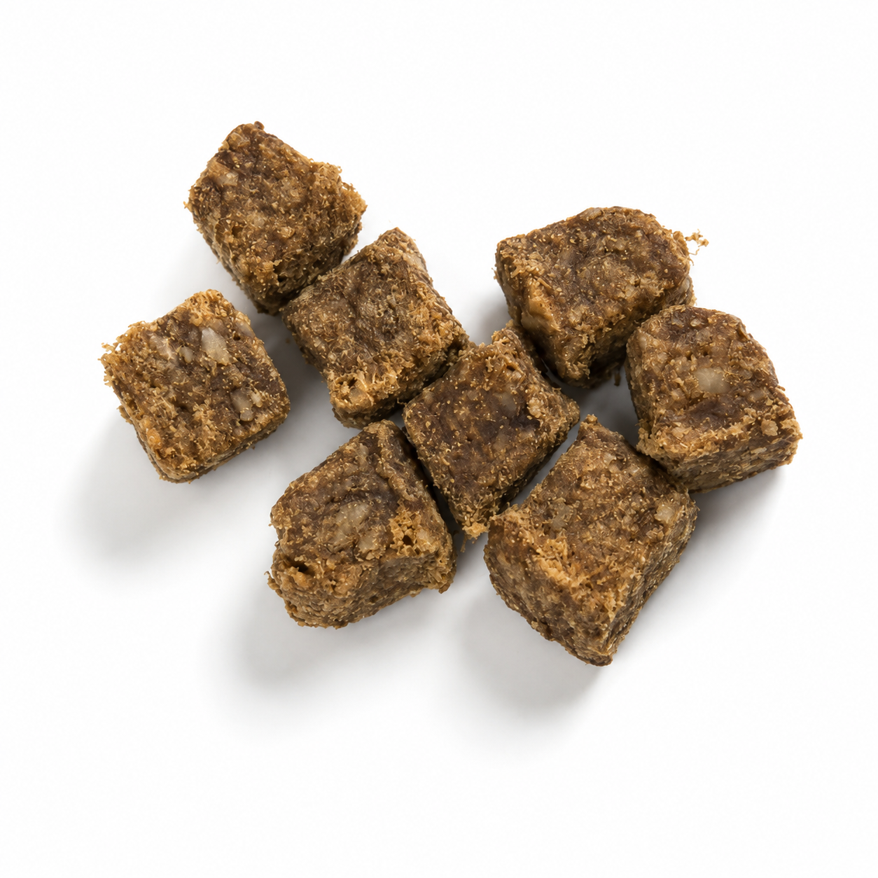 Sieben kleine, braune Hirschfleischwürfel mit grober, faseriger Struktur liegen locker auf einem weißen Hintergrund. Die getrockneten Hundesnacks werden durch weiche, natürliche Schatten hervorgehoben.