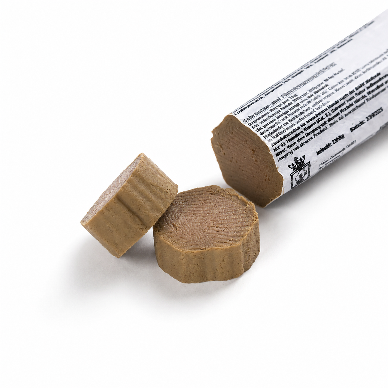 Eine Kalbsleberwurst für Hunde in weißer Verpackung liegt angeschnitten auf einem weißen Hintergrund. Vor der Wurst befinden sich zwei dicke Scheiben, die die feine, schnittfeste Konsistenz des Produkts zeigen. Weiche, natürliche Schatten sorgen für eine realistische Produktdarstellung.