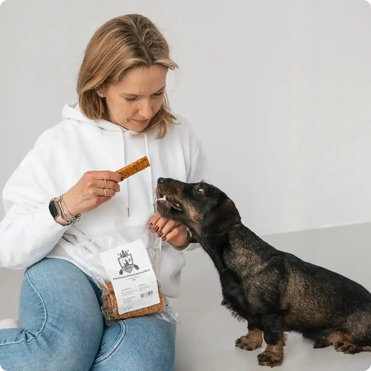 Frau gibt ihrem Dackel einen Snack von Royal Diamonds