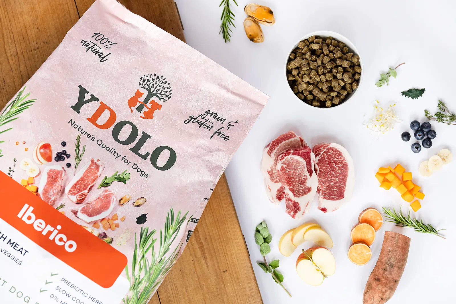 YDOLO Iberico Semi-Moist Hundefutter in roter Verpackung mit den natürlichen Nahrungsmittel und einem Napf mit den Kroketten im Hintergrund. Halbfeuchtes, getreide- und glutenfreies Hundefutter mit 75 % Frischfleisch, Monoprotein und präbiotischen Kräutern – geeignet für Hunde jeder Rasse.